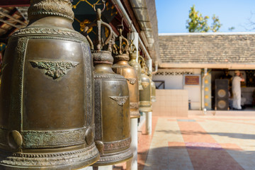 Outdoor sunny view of courtyard inside temple in Chiang Mai, Thailand, and selective focus view row of hanging antique brass bells, traditional religious instrument for asian and buddhism culture.