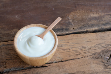 Natural homemade plain organic yogurt in wooden bowl and wood spoon on wood texture background