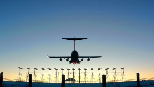 Four engine jet aircraft approaches runway for sunset landing, in slow motion.