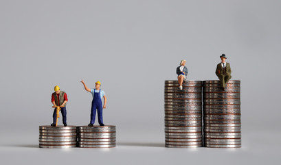 Miniature people with pile of coins. A concept of income disparity.