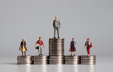 Miniature people with stack of coins. A concept of income inequality. - obrazy, fototapety, plakaty