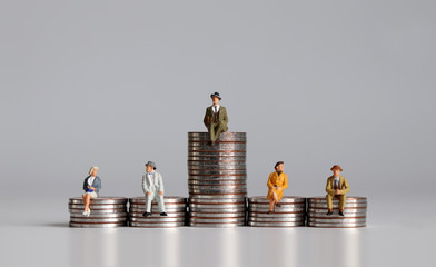 Miniature people with stack of coins. A notion of economic inequality.