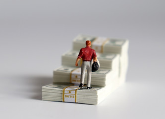 The back of a miniature man walking over a stack of cascaded bills.