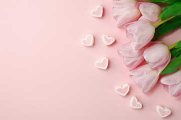Pastel pink tulip flowers bouquet and heart shaped candy on pink background. Flat lay, top view. Minimal floral springtime flatlay concept