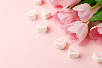 Pastel pink tulip flowers bouquet and heart shaped candy on pink background. Flat lay, top view. Minimal floral springtime flatlay concept