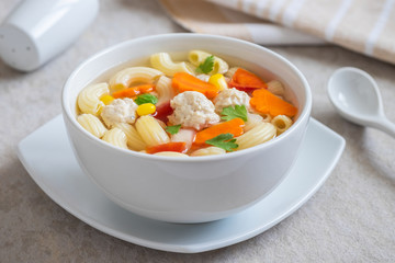 Macaroni chicken meatball soup in bowl .