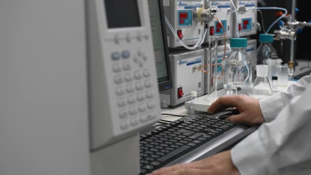 Scientist in a sterile white suit works on a computer in chemical laboratory. Laboratory assistant works with equipment. Science, biochemistry