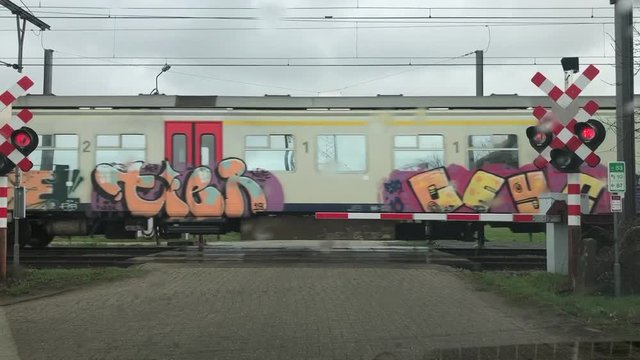 A passenger train crossing in font of a car on a rainy day