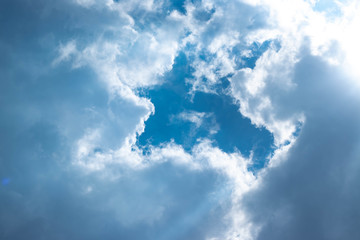 Blue sky with white clouds and gray cloud blue sky on a bright day with white clouds coming in floating come to cover sun causes a white beam causing beauty in the sky.