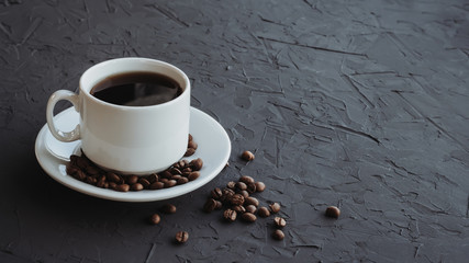 White cup of coffee and coffee beans on a dark background