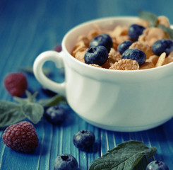 Cornflakes with berries raspberries and blueberries on blue wooden background. Top view.
