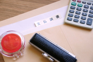 机の上の封筒の中の支払調書と印鑑と朱肉と電卓