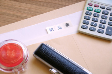 机の上の茶封筒の中の納品書と印鑑と朱肉と電卓