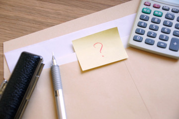 茶封筒に入った書類とはてなマークの書かれたメモと印鑑とペンと電卓