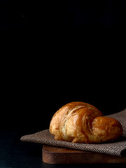 Croissant with icing on wood board in Chiaroscuro photo style, black background.