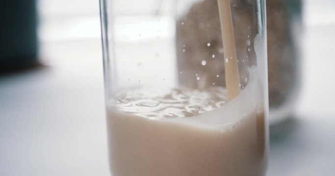 Close up of oat milk beverage pouring into drink glass bottle 