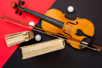 Violin, bow and books on a red-black background, top view