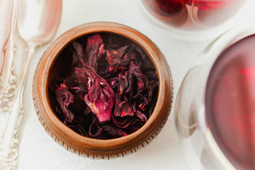 Dry flowers red hibiscus tea in a wooden  bowl close up on white background, view from the above