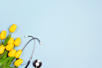 Bunch of yellow tulips and stethoscope on blue background with copy space. National Doctor's day.