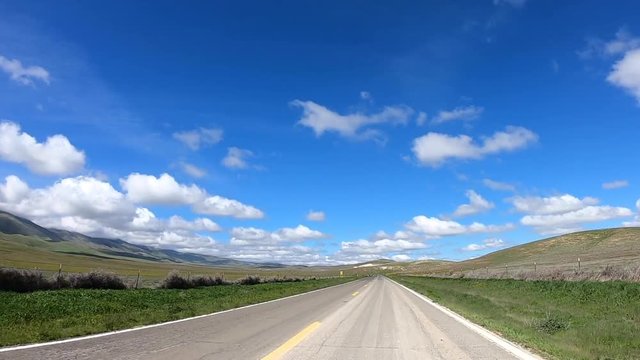 HD video driving POV down hwy 166 through green valleys on a windy road. Blue sky with white fluffy clouds. Picturesque green California after recent rains
