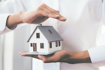 Saving money for house and real estate. Woman hand protecting on stack coins and house model on...