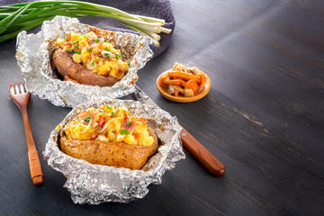 Baked potato in foil with bacon, onions and mushrooms on a gray wooden table. Copy space.