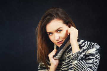 Studio portrait of a young woman on a dark background . The girl is dressed in a warm knitted sweater