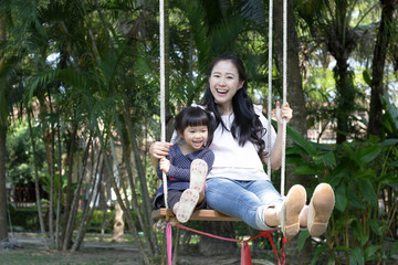 Mother plays swings with daughter in the garden.
