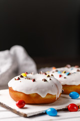 Cookery, baking and food concept - closeup. Donuts in white glaze with colored chocolate dragees on a decorative board on a dark background.