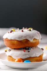 Cookery, baking and food concept - closeup. Two donuts in white glaze with color dragee on a plate.