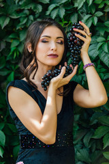 Portrait of young sexy brunette biting black grapes.