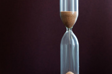 In the hourglass on a brown background, the sand of time quickly runs away.