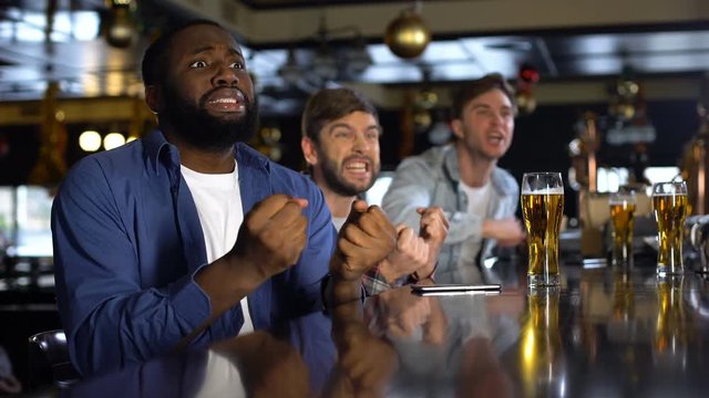 Multiracial male friends watching sport game, rejoicing victory, relaxing in bar