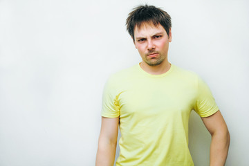 A disheveled displeased young man angrily reproachfully looks straight. A look from the underbelly, a conviction on white grey studio background.