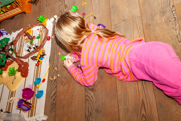 Little girl child playing with lots of colorful plastic toys on wooden floor indoors