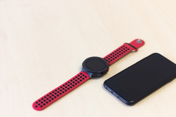 Red smart watch  and black smart mobile phone on wooden table.