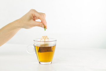 Closeup of a woman hand dipping a tea bag in a glass cup full of water with beautiful red-colored effects in the transparency of the water