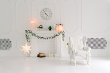 Bright white living room with a white armchair and fake fireplace, decorated with green leves