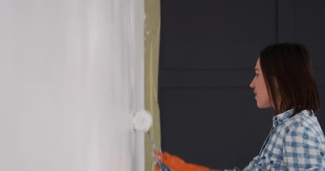 Young woman dancing and singing while painting wall at home