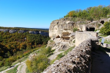 View of cavetown Chufut-Kale above autumn forest in valley near Bakhchisarai city on the Crimean Peninsula. It'is a medieval city-fortress in the Crimean Mountains that now lies in ruins.