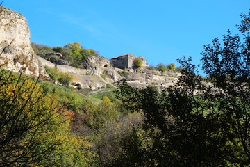 Fototapeta premium View from the valley on the cavetown Chufut-Kale in the autumn near Bakhchisarai city on the Crimean Peninsula. On the edge of the cliff are kenessas (East European Karaite or Persian synagogue).