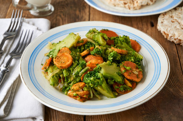 Fried broccoli with carrots and onions on a white plate