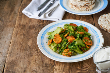 Fried broccoli with carrots and onions on a white plate