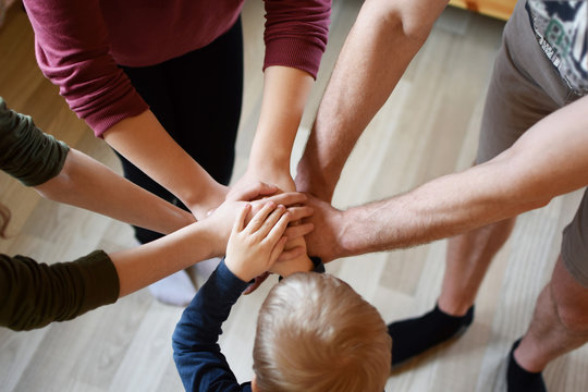 Stack of family people hands - father with children on light brown wooden texture laminate floor background indoors, little boy in middle. Family business, teamwork and unity concept.