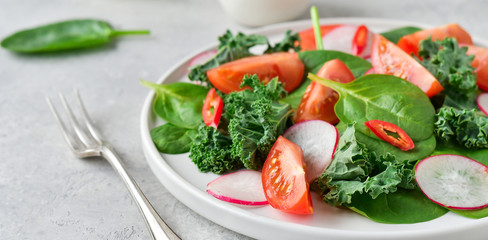 fresh salad of organic spinach, kale, tomatoes and radish with olive oil and lime juice. healthy eating concept. diet, vegan cuisine. light background, selective focus