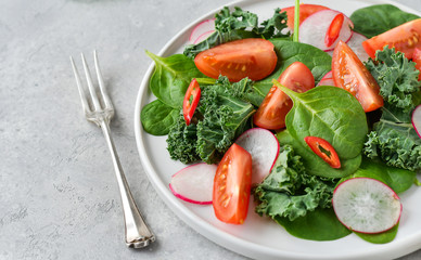 fresh salad of organic spinach, kale, tomatoes and radish with olive oil and lime juice. healthy eating concept. diet, vegan cuisine. light background, selective focus