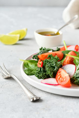 fresh salad of organic spinach, kale, tomatoes and radish with olive oil and lime juice. healthy eating concept. diet, vegan cuisine. light background, selective focus