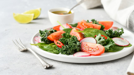 fresh salad of organic spinach, kale, tomatoes and radish with olive oil and lime juice. healthy eating concept. diet, vegan cuisine. light background, selective focus