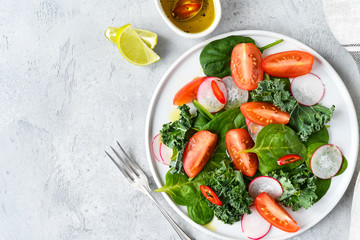 fresh salad of organic spinach, kale, tomatoes and radish with olive oil and lime juice. healthy eating concept. diet, vegan cuisine. light background, selective focus