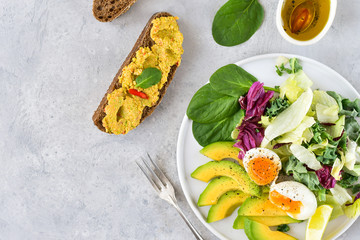 food for a healthy Breakfast or lunch. salad of avocado, kale leaves, egg and spinach, on a white plate, grain bread, diet food, organic vegetables, food flat lay